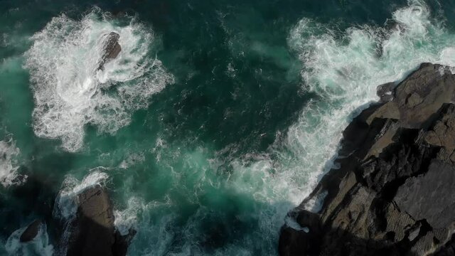 Huge cliffs in an overhead view, a blue sea with waves breaking with a lot of foam