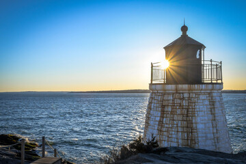 The setting sun shines behind a lighthouse in Rhode Island