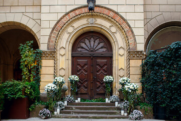 Obraz premium Wedding ceremony with natural white flowers against the background of a huge antique wooden door. On a wedding day in an old European city. Free space for text