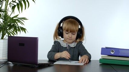 Teenage girl school student wearing wireless headphones calling to teacher on laptop. Distance education learning at home. Teen schoolgirl chatting by web cam preparing for test or exam