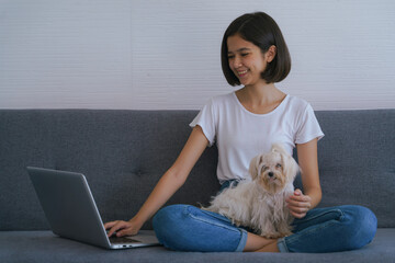 asian young women playing with small dog while working with laptop