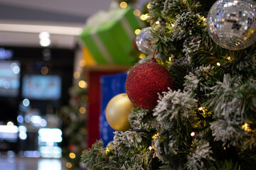 Closeup medium red balls Christmas tree decorated with small bulbs is beautiful. Christmas tree decoration with white snow, copy space on left for design or text, blurred background, beautiful bokeh.