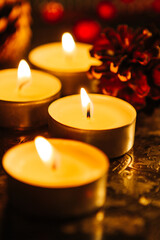 Several burning candles on a silver tray with pine cones and holly berries in the background