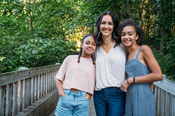 Portrait of mom hugging happy teen daughters outside