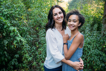 Portrait of mom hugging happy teen daughters outside