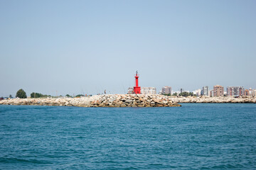 Fototapeta na wymiar red lighthouse seen from the sea, on the rocks of the coast, with the blue sea and the clear sky on a summer day