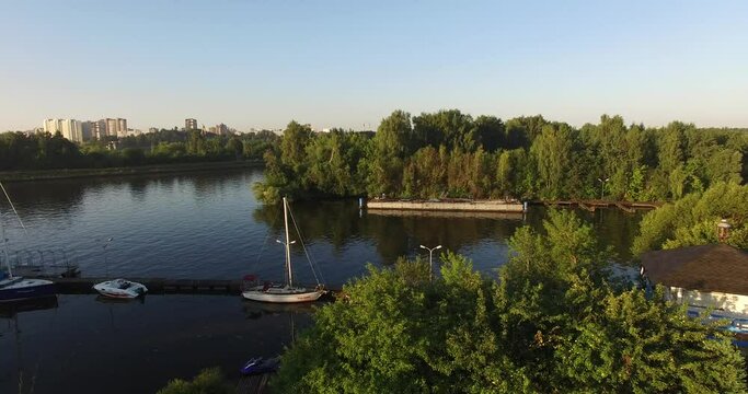 4K high quality calm windless bright summer morning aerial video of Moscow Channel yacht club embankment, green trees, wooden pier and shore with moored anchored boats and yachts near Moscow, Russia