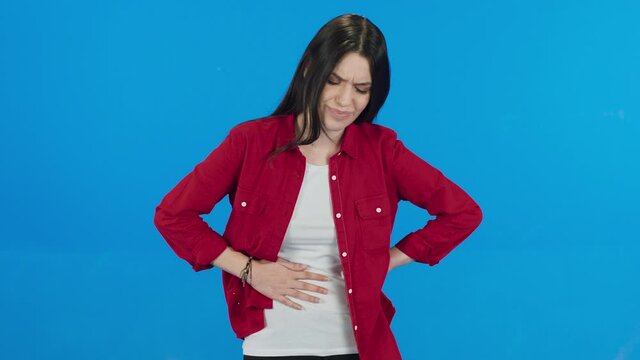 Female suffering from digestive problems. Bearded woman wearing white t-shirt sudden stomach ache, severe abdominal pain, constipation, gastritis, pancreatic diseases. Blue background.