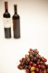 Obraz premium Champagne grape and Red Globe grape in front with 2 blurred wine bottles in the background on a white background.