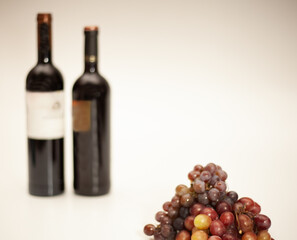 Obraz premium Champagne grape and Red Globe grape in front with 2 blurred wine bottles in the background on a white background.