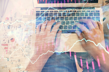 Double exposure of man's hands typing over laptop keyboard and forex chart hologram drawing. Top view. Financial markets concept.