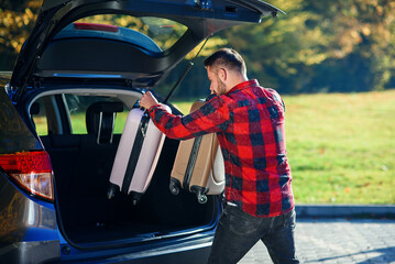 Young man unloads luggage out of the SUV after coming back home from summer family vacation.