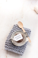 An isolated chocolate mousse covered jar on a knitted blue cloth with tag on the cover and a wooden spoon next to the jar.