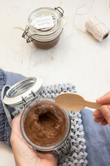 A left hand holding an opened chocolate mousse jar and another hand holding a spoon ready to eat the mousse.