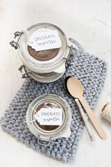 Two chocolate mousse covered jars on a knitted blue cloth with a couple of spoons and two tags.