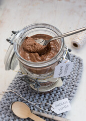 Closeup view of an isolated chocolate mousse jar with a spoon full of mousse at the top of it on a blue knitted napkin.