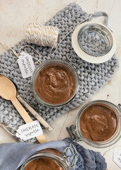 Two chocolate mousse jars and a half on a knitted blue cloth surrounded by a couple of spoons and two tags.