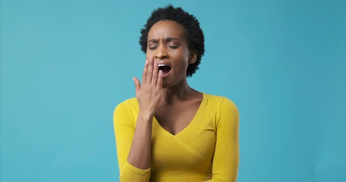 Tired african american woman yawning over blue background