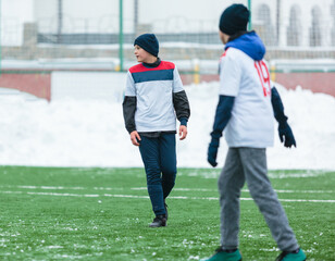 Boys in white sportswear running on soccer field with snow on background. Young footballers dribble and kick football ball in game. Training, active lifestyle, sport, children winter activity