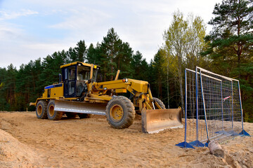 Obraz na płótnie Canvas Motor Grader on road construction in forest area. Greyder leveling the sand, ground and gravel during road work. Heavy machinery and construction equipment for grading. Earthworks grader machine