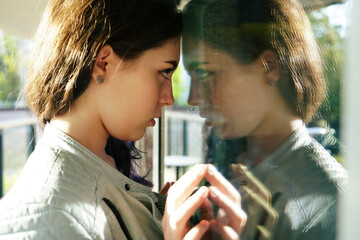 Self reflection portrait of amazing young girl in mirrored window. Unusual strange pretty woman...