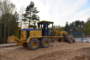 Obraz na płótnie Canvas Motor Grader on road construction in forest area. Greyder leveling the sand, ground and gravel during road work. Heavy machinery and construction equipment for grading. Earthworks grader machine