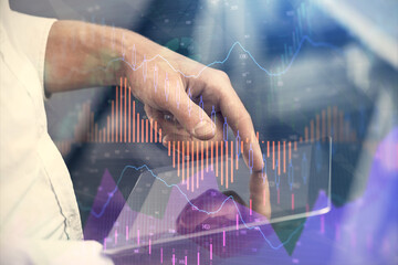 Double exposure of man's hands holding and using a digital device and forex graph drawing. Financial market concept.