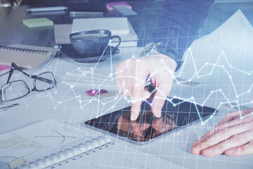 Double exposure of man's hands holding and using a digital device and forex graph drawing. Financial market concept.