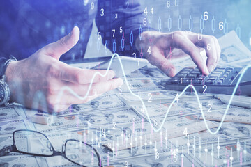 Double exposure of man's hands holding and using a digital device and forex graph drawing. Financial market concept.