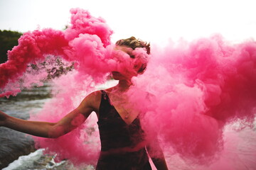 Image of a woman holding a pink smoke grenade while the smoke hides her face and identity. 