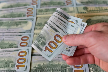 Stack Of 100 Dollars Banknotes Bundles in a man's hand against the background of American banknotes