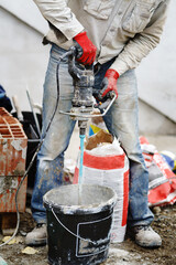 Close up on midsection of unknown man using hand electric drill mixer to prepare adhesive cement...