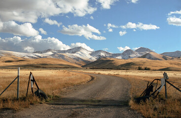 Montana Ranch entrance with road, hills, snow, and sky. - obrazy, fototapety, plakaty
