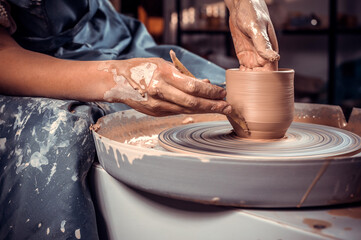 Close-up A woman potter in beautifully sculpts a deep bowl of brown clay and cuts off excess clay on a potter's wheel in a beautiful workshop