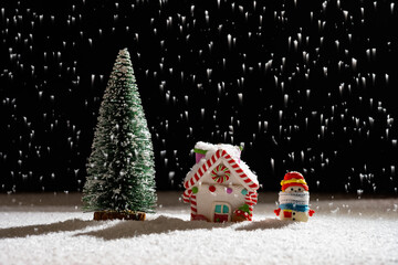 Christmas house and fir tree and a snowman with medical mask in a snowing night