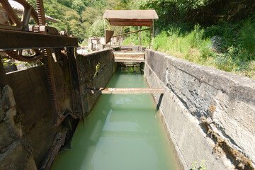The construction of an old abandoned hydroelectric power plant on a clear day, below the artificial creek