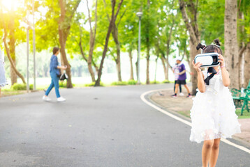 Obraz premium Blur background.Outdoor park green child wear white dress beautiful is playing joystick virtual reality video vr game cyberspace entertainment technology innovation future digital simulation 