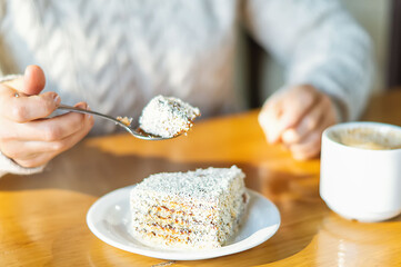 Women's hands in a warm knitted sweater in a city cafe with a teaspoon cut off a piece of delicious cake. Coffee mug on the table. Rest in a coffee shop. Close-up, selective focus.