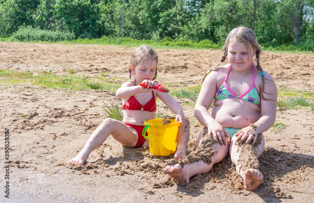 Wall mural Girls play on the sandy beach by the lake in the summer heat. 