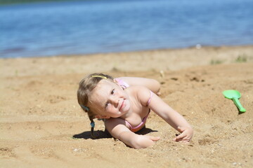 	A girl is sunbathing on a sandy beach on the lake in the summer heat.