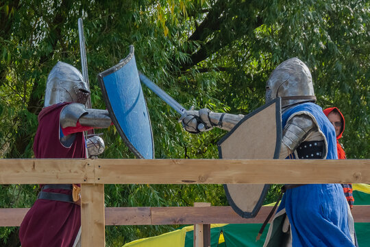Tver / Russia - September 29 2020: Warriors in heavy armor fight with swords. In the background, the referee and spectators. Historical reconstruction of medieval European knightly tournaments