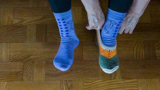 Elderly woman tries on leg sock from wool yarn which she is knitting using knitting needles