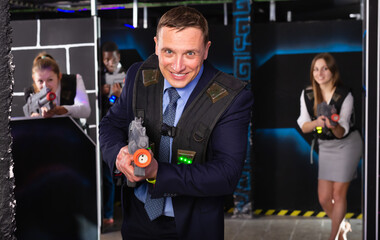 Man in the business suit holding a laser gun and playing laser tag with colleagues