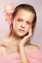 Young beautiful woman with perfect skin and a flower in her hair on pink background