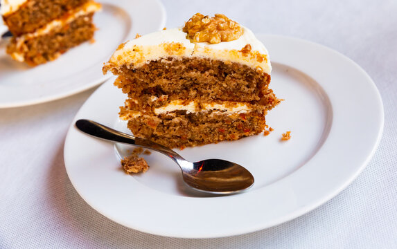 Slice of soft carrot cake with cream cheese glaze on wooden table. High quality photo