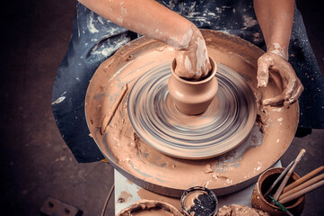 Young woman master works with clay on a potter's wheel. Making ceramic dishes. Close-up.