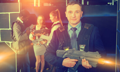 Man in a business suit holding a laser gun and playing laser tag with colleagues