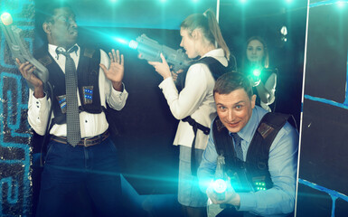 Happy cheerful smiling men and women in business suits playing laser tag emotionally in dark room