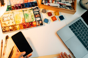 Flat lay- Water colour artist working desk with mock up paper and smartphone for finding reference.