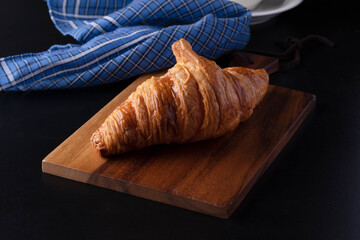 Croissant on a wooden cutting board on a black background